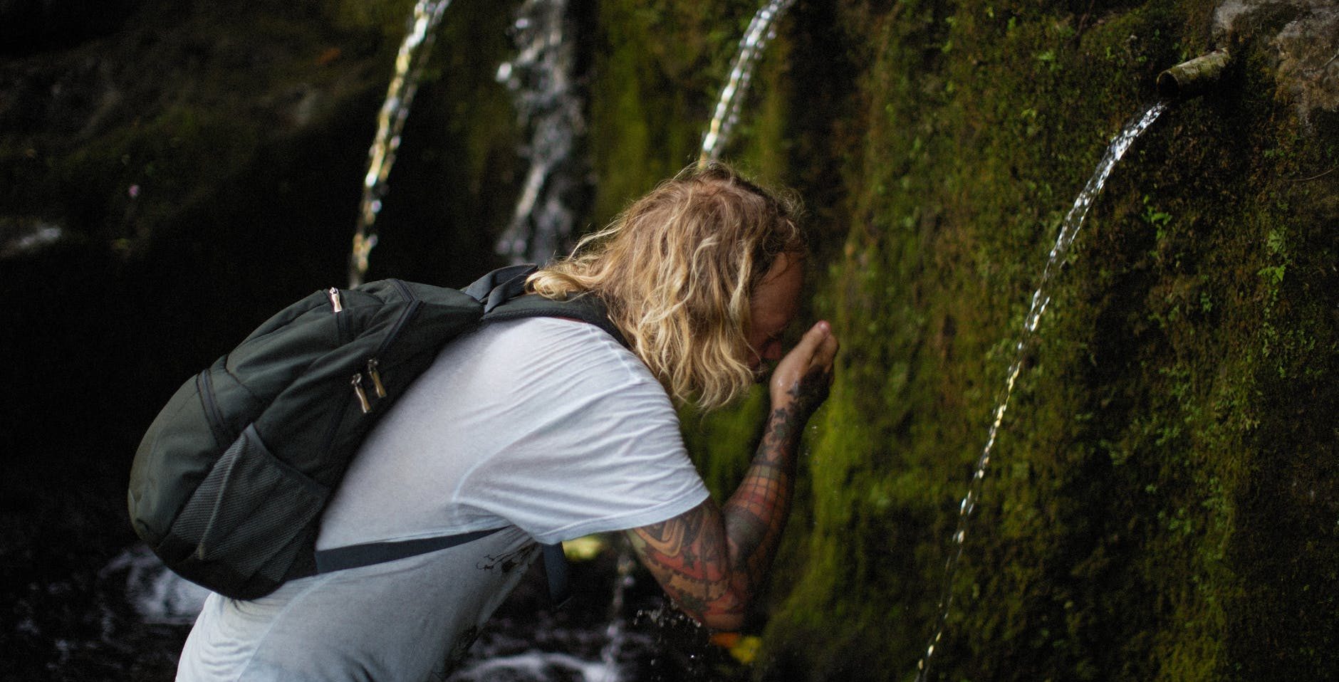 a hiker washing his face on the flowing water of a waterfalls