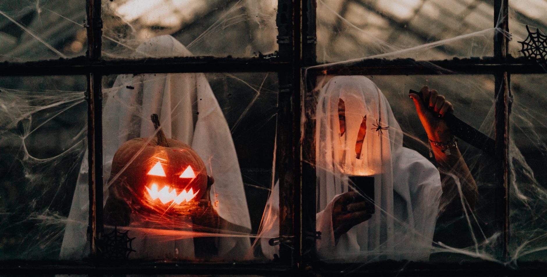 two people in ghost costumes standing beside an illuminated jack o lantern