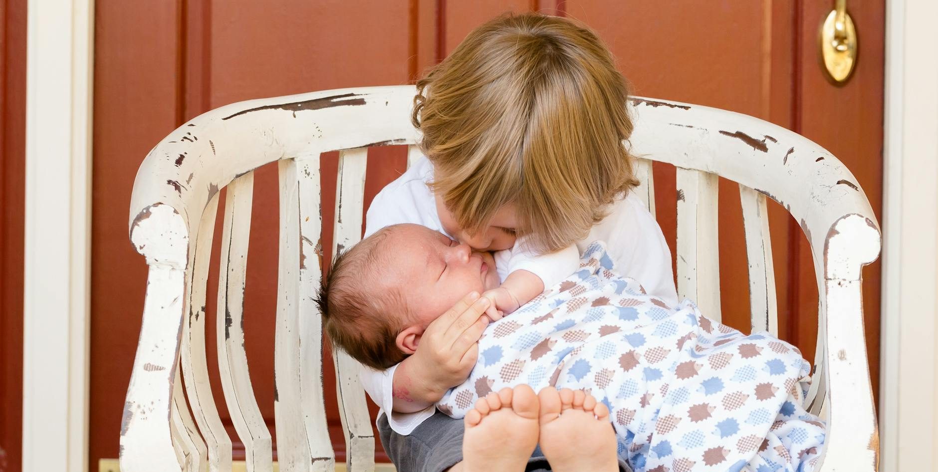 boy carrying and kissing baby sitting on chair