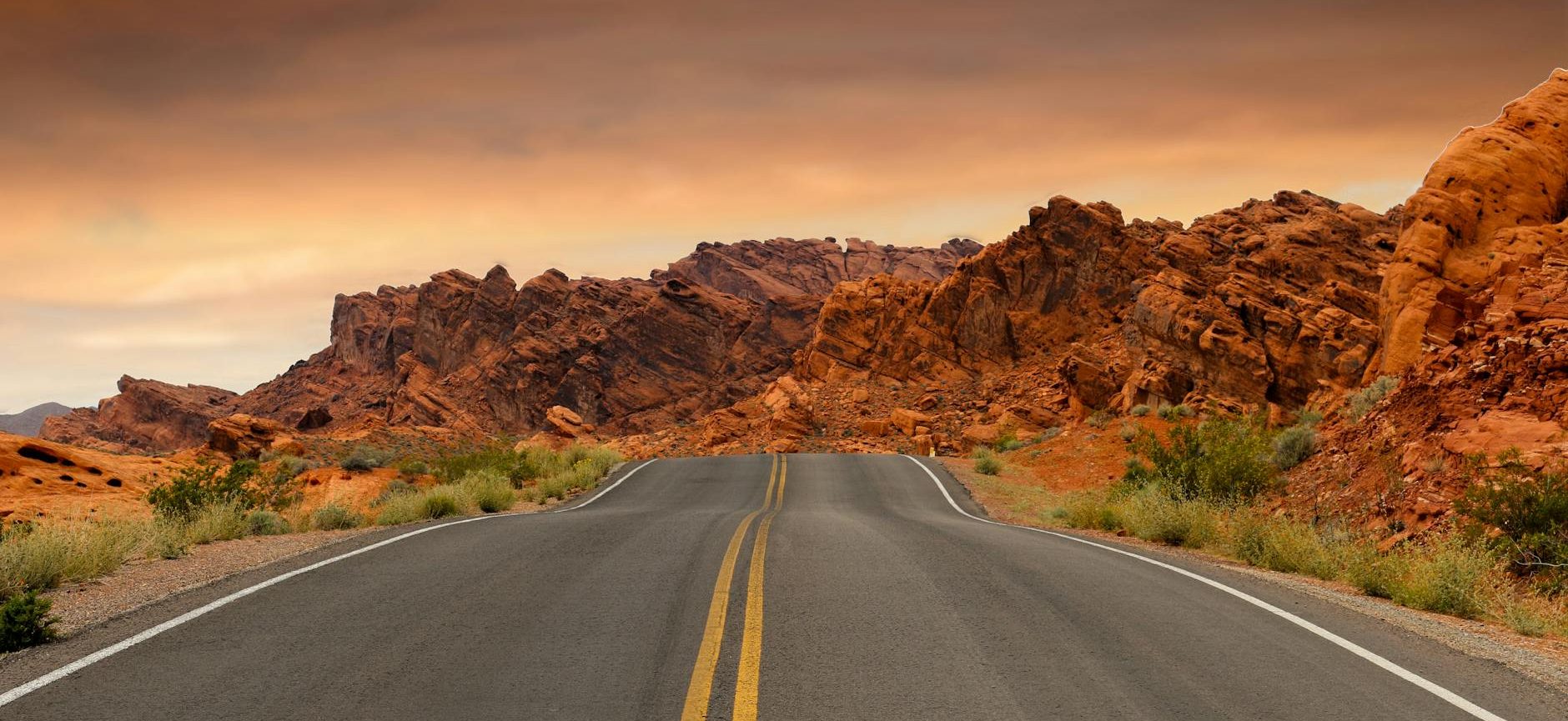 gray concrete road beside brown mountain during golden hour